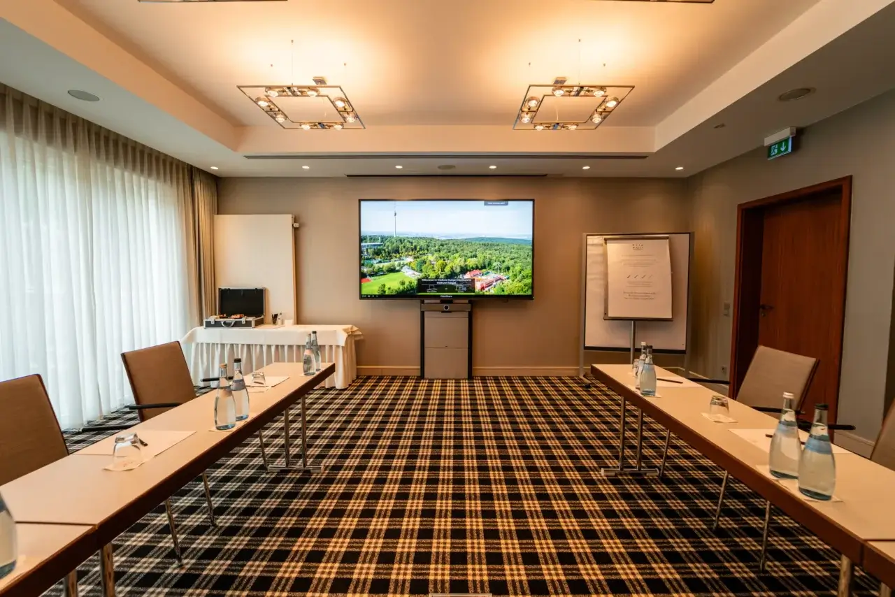 Ein moderner Konferenzraum mit einem großen Bildschirm, Besprechungstischen und ergonomischen Stühlen.
