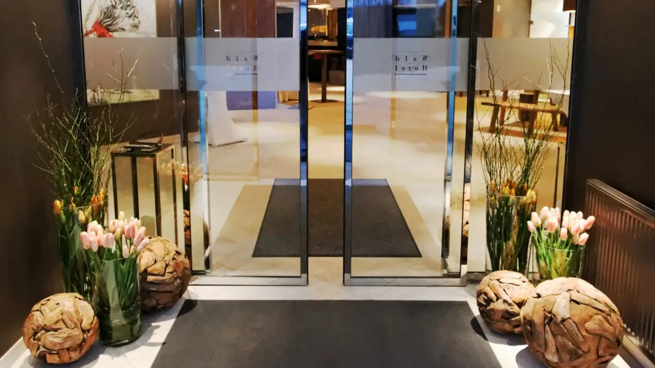 Eleganter Hoteleingang mit Glas­türen, stilvoller Dekoration und frischen Blumen.