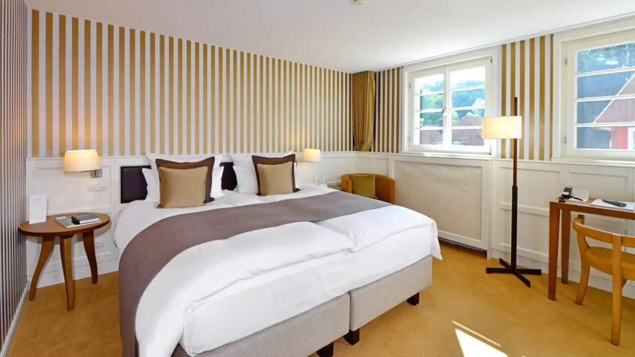 Blick auf ein frisch bezogenes Bett im Waldhotel Stuttgart mit einer gold gestreiften Wandtapete.