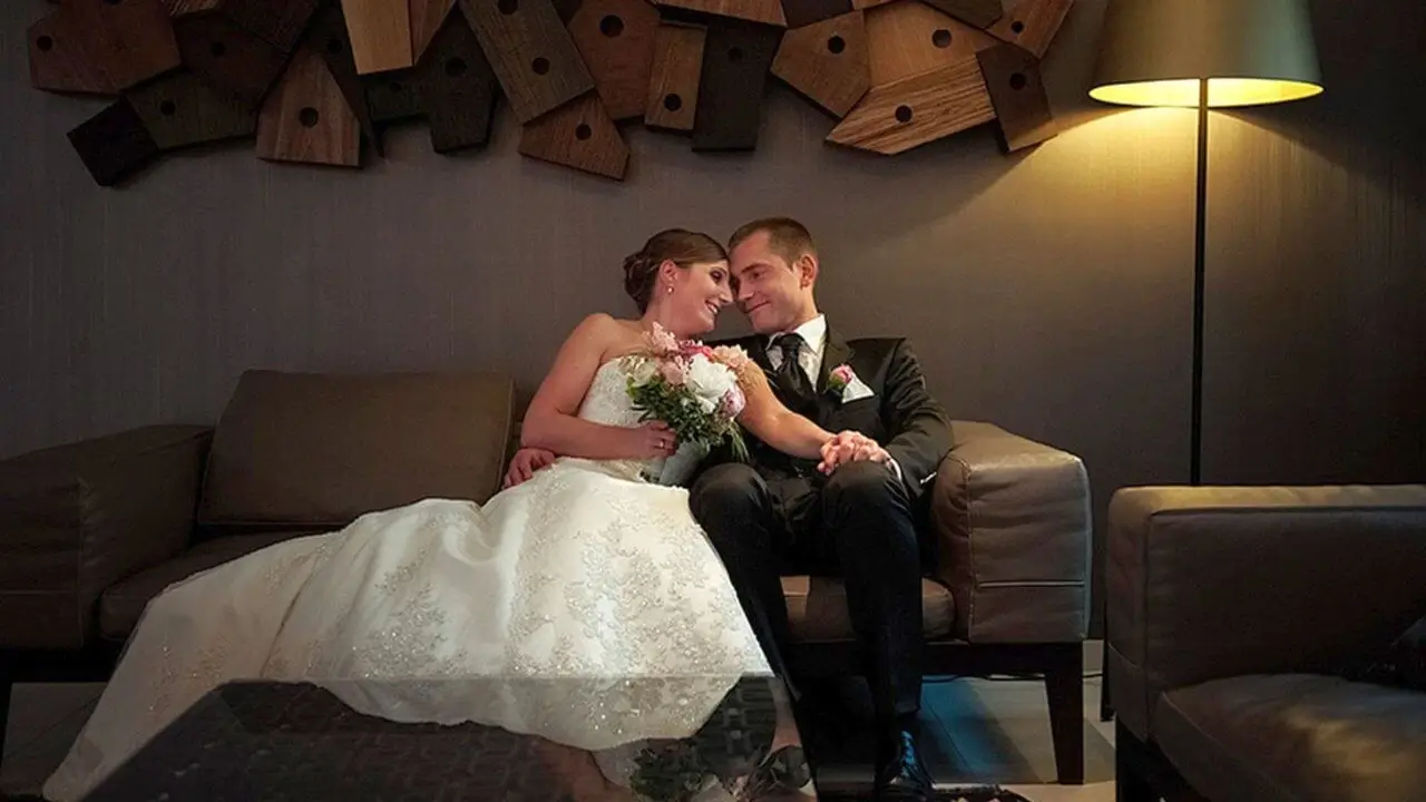 Ein glückliches, frisch verheiratetes Ehepaar sitzt in Hochzeitskleidung auf einer braunen Couch einer Hochzeitslocation in Stuttgart.