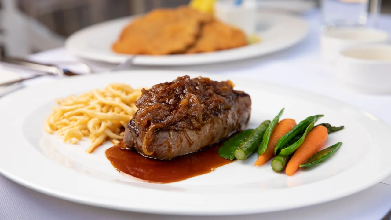 Saftiges Rindersteak mit Röstzwiebeln, begleitet von Spätzle und gedünstetem Gemüse im Gourmet Restaurant mit Terrase in Stuttgart.