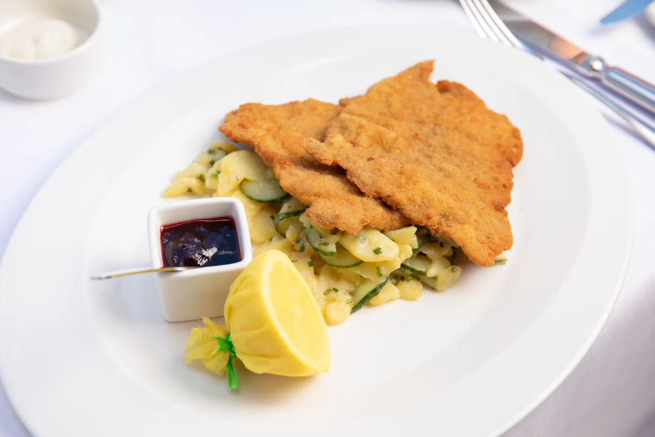Ein knuspriges Schnitzel auf Kartoffelsalat mit Preiselbeeren und Zitronenscheibe.