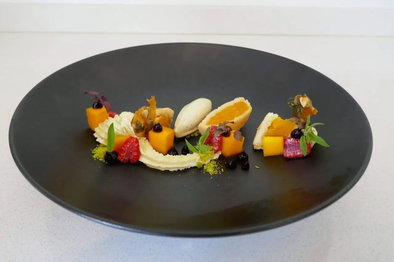 Kunstvoll angerichtetes Dessert mit frischen Früchten und Creme auf einem schwarzen Teller.