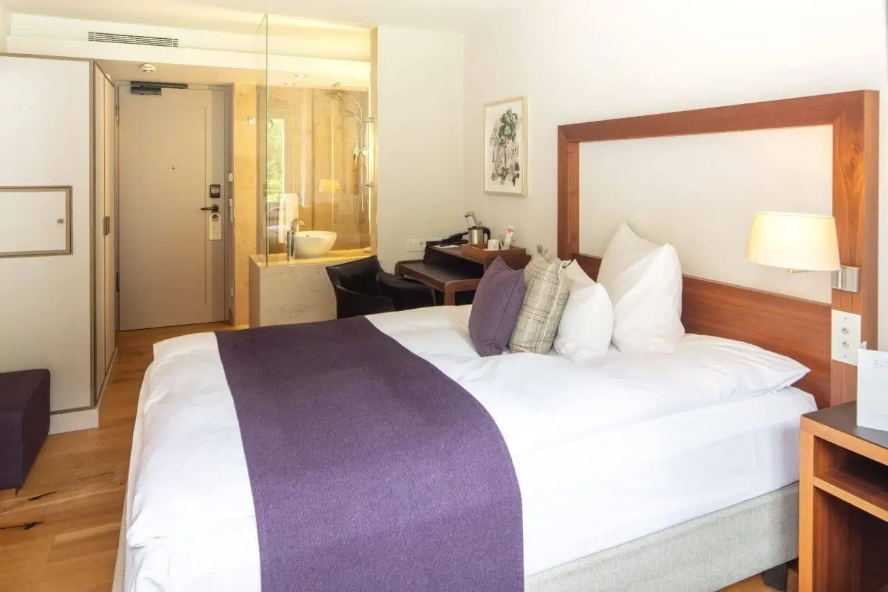 EIn modernes Hotelzimmer mit eleganter Einrichtung, Holzdetails und offener Dusche.
