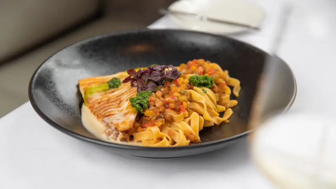 Ein Teller mit gegrilltem Fischfilet auf Tagliatelle und Gemüseragout, garniert mit frischen Kräutern.