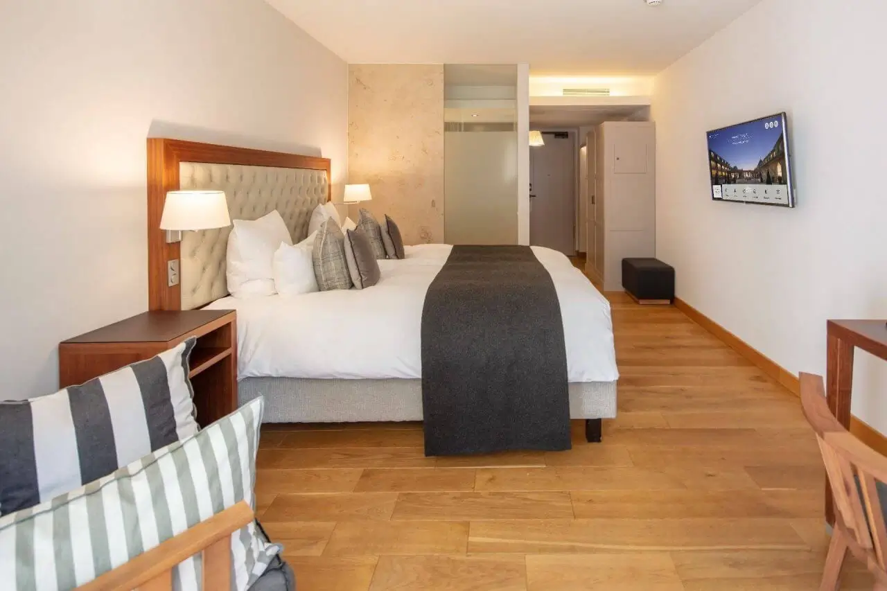 Ein modernes stillvolles Hotelzimmer mit großem Doppelbett, eleganten Nachttischen, Holzboden und Flachbildfernseher an der Wand., perfekt für eine Übernachtung in Stuttgart.