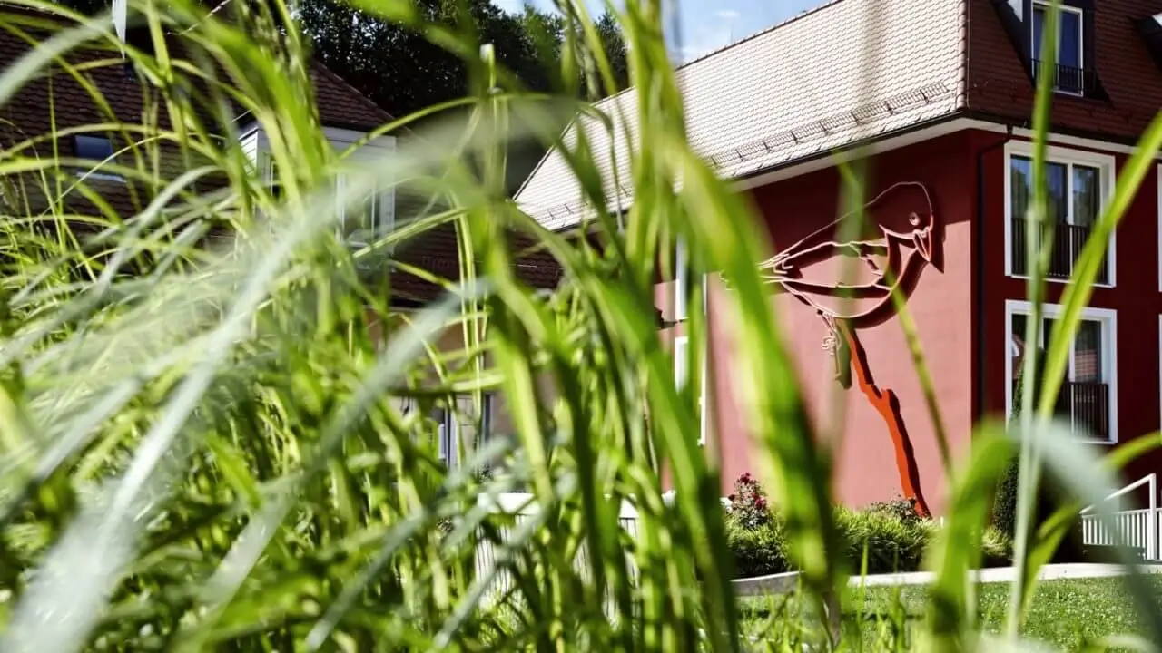 Gras im Vordergrund, rotes Gebäude mit Vogelsilhouette – Firmenfeier in Stuttgart.