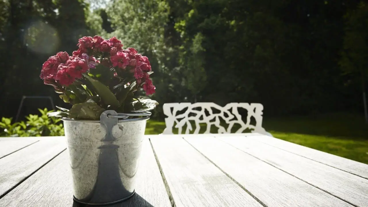 Eine Nahaufnahme eines Blumenarrangements in einem Metalltopf auf einem Holztisch in einem sonnigen Garten im Waldhotel Stuttgart.