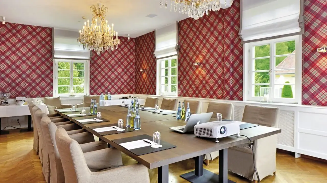 Ein eleganter Tagungsraum im Waldhotel Stuttgart, ausgestattet mit einem langen Konferenztisch, bequemen Stühlen, einem Projektor und Mineralwasserflaschen.