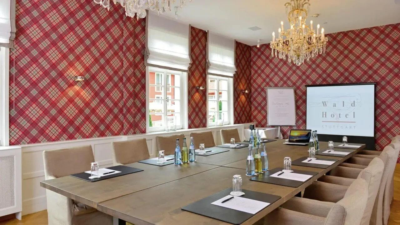 Ein stilvoller Tagungsraum im 4 Sterne Tagungshotel in Stuttgart mit einem großen Besprechungstisch, bequemen Polsterstühlen, einer Projektionsleinwand und Mineralwasserflaschen.