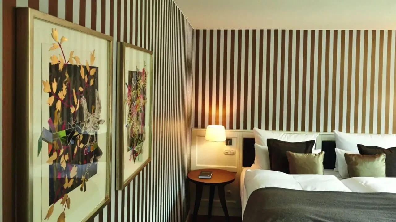 Tagungsraum Stuttgart: Modernes Hotelzimmer mit gestreifter Tapete, stilvollen Kunstwerken und gemütlichem Doppelbett.