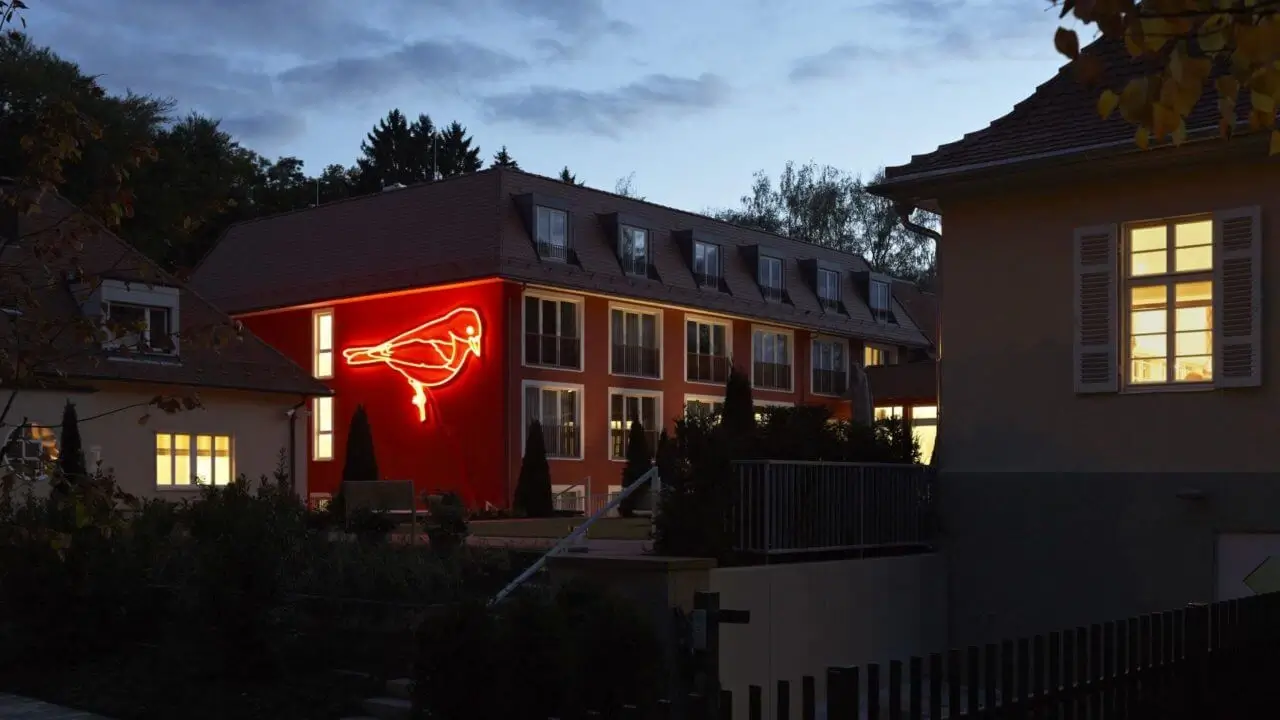 Ein beleuchtetes Gebäude bei Dämmerung mit leuchtender Vogel-Neoninstallation an der Fassade.