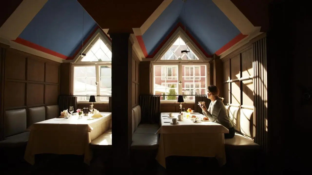 Gemütliche Nische im Gourmet Restaurant Finch in Stuttgart mit hohen Fenstern, an denen eine Frau alleine bei Tageslicht frühstückt.