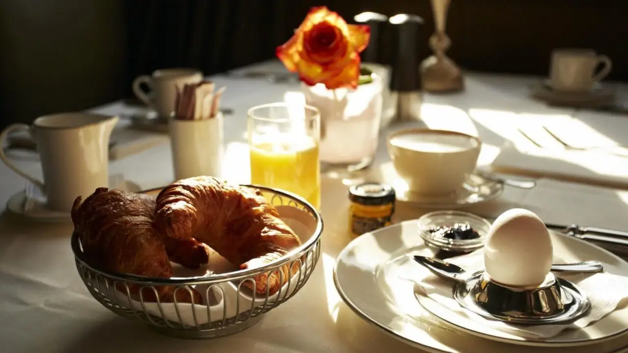Ein Frühstückstisch mit Croissants, frisch gepresstem Orangensaft, einem gekochten Ei und einer Tasse Kaffee.