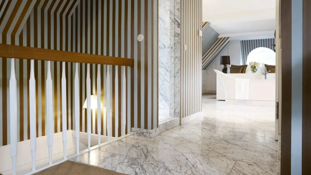 Ein eleganter Raum mit gestreiften Wänden, marmoriertem Boden und einer modernen Treppe, die zu einem hellen Bereich führt.