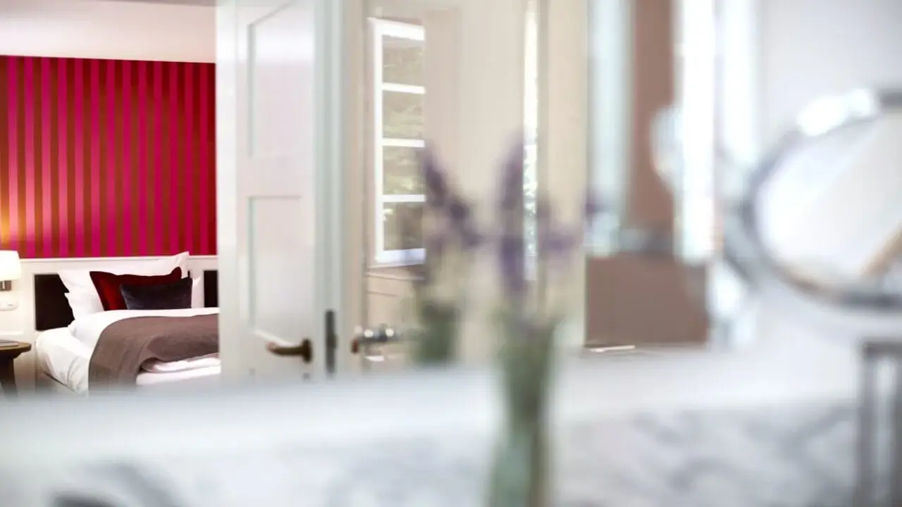 Blick durch eine geöffnete Tür in ein stilvoll eingerichtetes Hotelzimmer mit rot gestreifter Wand, einem bequemen Bett und eleganter Dekoration im Waldhotel Stuttgart.
