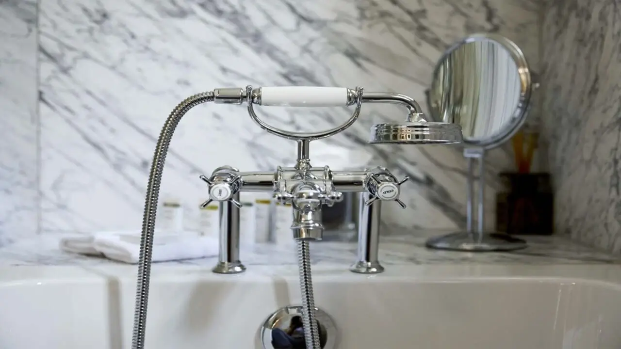Detailaufnahme einer eleganten Armatur im Marmorbad des Waldhotels Stuttgart, mit verchromtem Design und einem runden Schminkspiegel im Hintergrund.