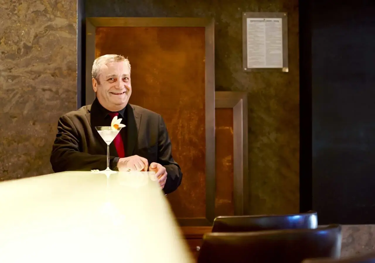 Ein lächelnder Mitarbeiter eines Hotels, vor dem ein eleganter Drink steht.